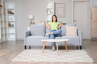 Oturma odasındaki gri kanepede dinlenen genç kadın.