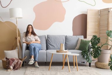 Oturma odasındaki gri kanepede oturan genç kadın.