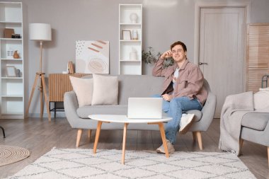 Oturma odasındaki gri koltukta oturan genç adam.