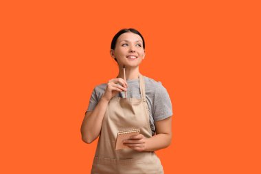 Turuncu arka planda not defteri olan güzel bir garson kız.