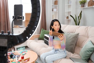 Kadın Asyalı güzellik blogcusu evde video kaydederken göz farı uyguluyor