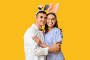 Sarı arka planda Paskalya tavşanı kulakları olan mutlu genç çift.