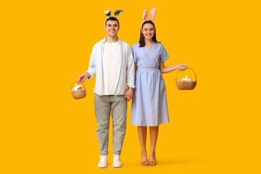 Paskalya sepetleri ve sarı arka planda tavşan kulakları olan mutlu genç çift.