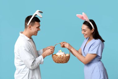 Mavi arka planda Paskalya tavşanı kulakları ve sepeti olan mutlu genç çift.