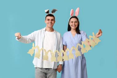 Mavi arka planda Paskalya tavşanı kulakları ve çelengi olan mutlu genç çift.