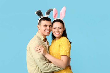 Mavi arka planda Paskalya tavşanı kulakları olan mutlu genç çift