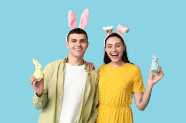 Paskalya tavşanı kulakları ve mavi arka planda oyuncak tavşanları olan mutlu genç çift.