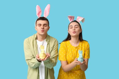 Paskalya tavşanı kulakları ve mavi arka planda oyuncak tavşanları olan mutlu genç çift.