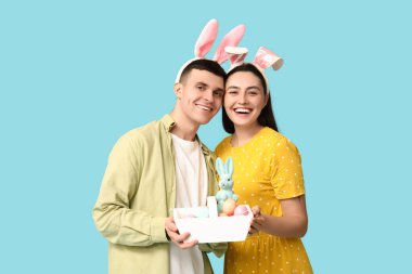 Tavşan kulaklı mutlu genç çift ve mavi arka planda Paskalya sepeti