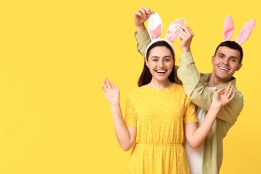 Sarı arka planda Paskalya tavşanı kulakları olan mutlu genç çift.