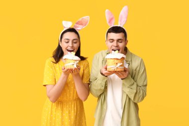 Paskalya tavşanı kulaklı mutlu genç çift ve sarı arka planda pastalar.