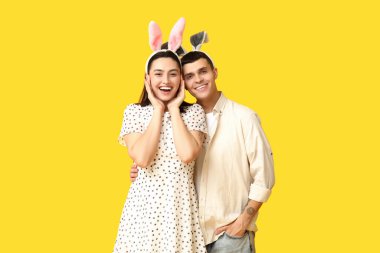 Sarı arka planda Paskalya tavşanı kulakları olan mutlu genç çift.