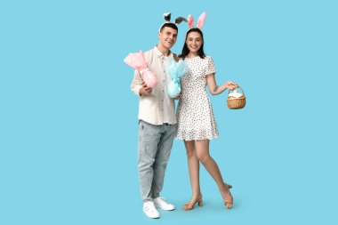 Paskalya tavşanı kulaklı, sepetli ve mavi arka planda hediyeleri olan mutlu genç çift.