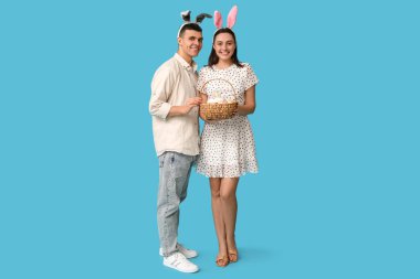 Paskalya sepeti ve mavi arka planda tavşan kulaklı mutlu genç çift.