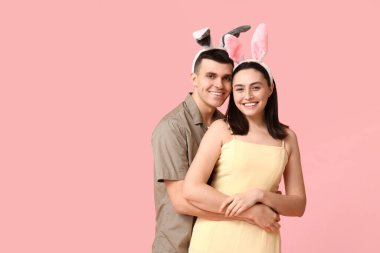 Pembe arka planda Paskalya tavşanı kulakları olan mutlu genç çift.