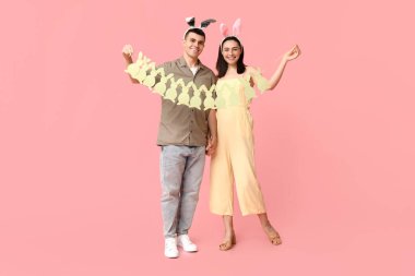 Paskalya çelengi ve pembe arka planda tavşan kulaklı mutlu genç çift.