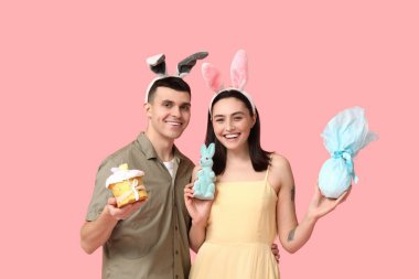 Paskalya pastası, tavşan kulağı, hediye ve pembe arka planda oyuncak tavşan olan mutlu genç çift.