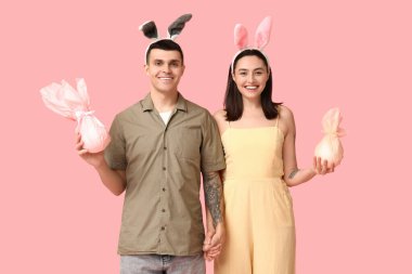 Paskalya hediyeleri ve pembe arka planda tavşan kulaklı mutlu genç çift.