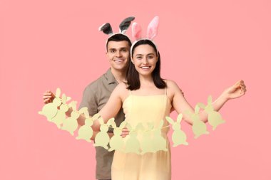 Paskalya çelengi ve pembe arka planda tavşan kulaklı mutlu genç çift.