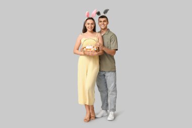 Paskalya sepeti ve gri arka planda tavşan kulaklı mutlu genç çift.