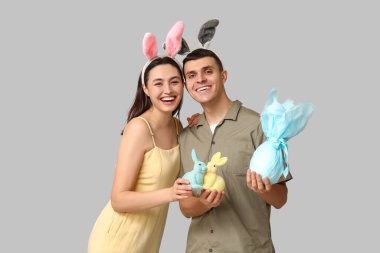 Paskalya tavşanı kulaklı mutlu bir çift hediye ve gri arka planda oyuncak tavşanlar.