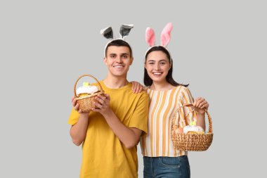 Paskalya sepetleri ve gri arka planda tavşan kulakları olan mutlu genç çift.