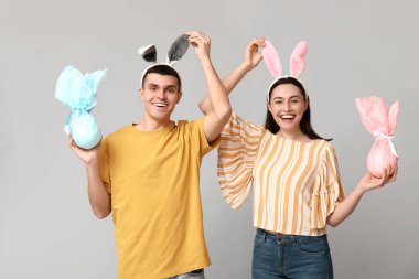 Paskalya tavşanı kulaklı mutlu genç çift ve gri arka planda hediyeler