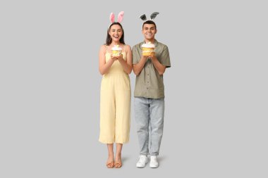 Paskalya pastaları ve gri arka planda tavşan kulaklı mutlu genç çift