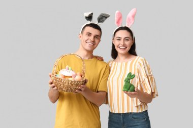 Paskalya sepeti, oyuncak tavşan ve gri arka planda tavşan kulaklı mutlu genç çift.
