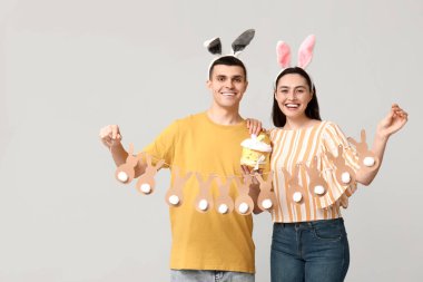 Paskalya pastası, çelenk ve gri arka planda tavşan kulaklı mutlu çift