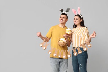Paskalya pastası, çelenk ve gri arka planda tavşan kulaklı mutlu genç çift.
