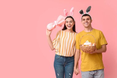 Paskalya sepeti, tavşan kulakları ve pembe arka planda hediyeleri olan mutlu genç çift.