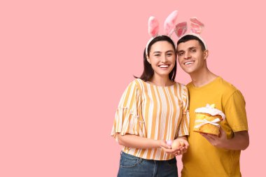 Paskalya pastası, yumurta ve pembe arka planda tavşan kulaklı mutlu çift.