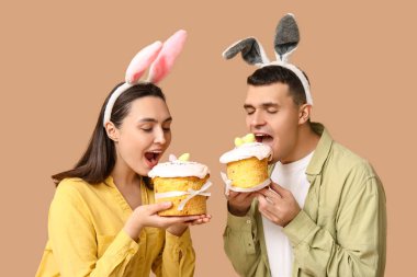 Paskalya tavşanı kulaklı mutlu genç çift bej arka planda pasta yiyor.