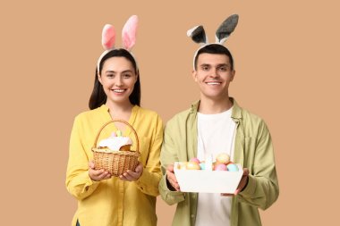 Paskalya sepetleri ve bej arka planda tavşan kulakları olan mutlu genç çift.