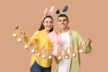 Paskalya çelengi, hediye ve bej arka planda tavşan kulaklı mutlu genç çift.