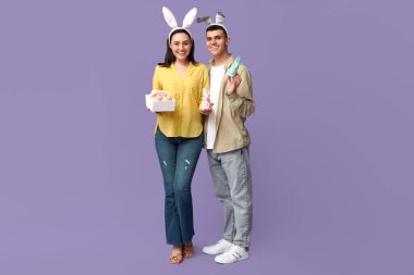 Paskalya sepeti, oyuncak tavşanlar ve leylak arka planda tavşan kulakları olan mutlu genç çift.