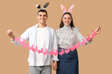 Paskalya çelengi ve bej arka planda tavşan kulaklı mutlu genç çift.