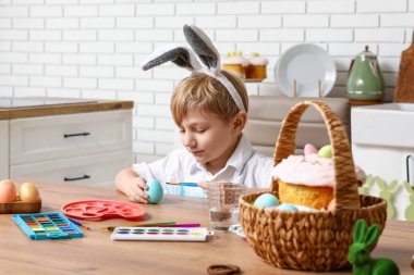 Tavşan kulaklı şirin çocuk evde paskalya yumurtası boyuyor.