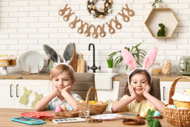 Mutfaktaki masada boyalı tavşan kulağı ve sepet sepet paskalya yumurtası takan şirin çocuklar.