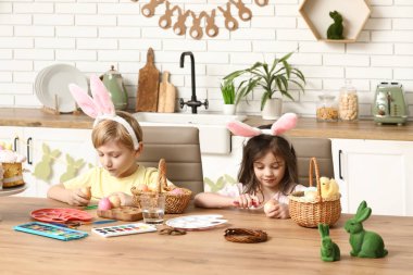 Tavşan kulaklı şirin çocuklar Paskalya yumurtalarını evde boyuyor.