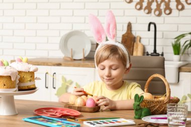 Tavşan kulaklı şirin çocuk evde paskalya yumurtası boyuyor.