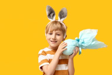 Sarı arka planda Paskalya hediyesi yumurtası olan tavşan kulaklı şirin bir çocuk.