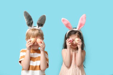 Mavi arka planda Paskalya yumurtaları olan tavşan kulaklı küçük bir çocuk.