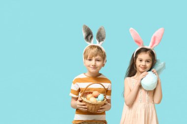 Paskalya yumurtası sepeti ve mavi arka planda hediyesiyle tavşan kulaklı şirin bir çocuk.