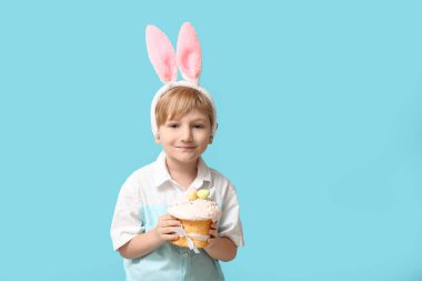Mavi arka planda Paskalya pastası olan tavşan kulaklı şirin bir çocuk.