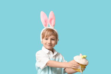 Mavi arka planda Paskalya pastası olan tavşan kulaklı şirin bir çocuk.