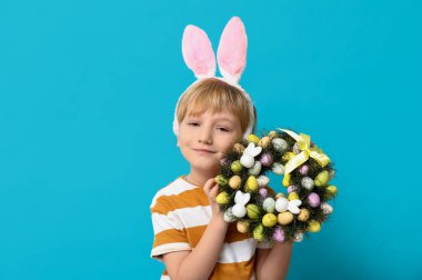 Mavi arka planda Paskalya çelengi olan tavşan kulaklı şirin bir çocuk.