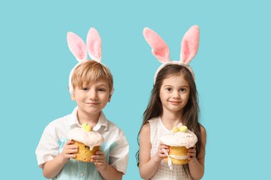 Mavi arka planda Paskalya pastaları olan tavşan kulaklı şirin çocuklar.