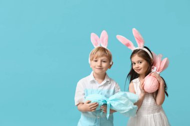 Mavi arka planda Paskalya hediyesi yumurtaları olan tavşan kulaklı şirin çocuklar.